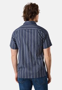 Korte mouwen overhemd met verticale marineblauwe en witte strepen, een kraag en een rechte zoom. Gemaakt van lichtgewicht stof.