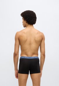 Μαύρα ανδρικά boxer με μπλε ζώνη μέσης που φέρει το λογότυπο "TOMMY HILFIGER". Το ύφασμα φαίνεται λείο και εφαρμοστό, προσφέροντας έναν μινιμαλιστικό σχεδιασμό.