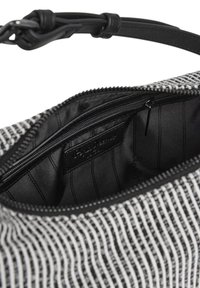Interno della borsa a righe bianche e nere, caratterizzato da una fodera nera liscia, una tasca con zip e un'etichetta con testo. I bordi sono rifiniti in modo ordinato.
