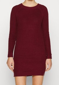 Abito in maglia color bordeaux con maniche lunghe, scollo a giro, texture a costine e spacchi laterali, che offre una silhouette aderente.
