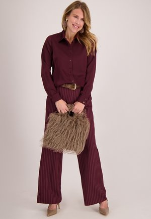 Bordeauxrood overhemd met knopen, brede gestreepte broek, bruine riem, handtas met bonttextuur in beige en beige schoenen met hak. Gladde stof, losse pasvorm.