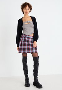 Szürke textúrájú crop top ezüst csattal, kockás bővülő szoknya és magas fekete bőr csizmák vastag talppal. Fekete bolyhos kardigán.