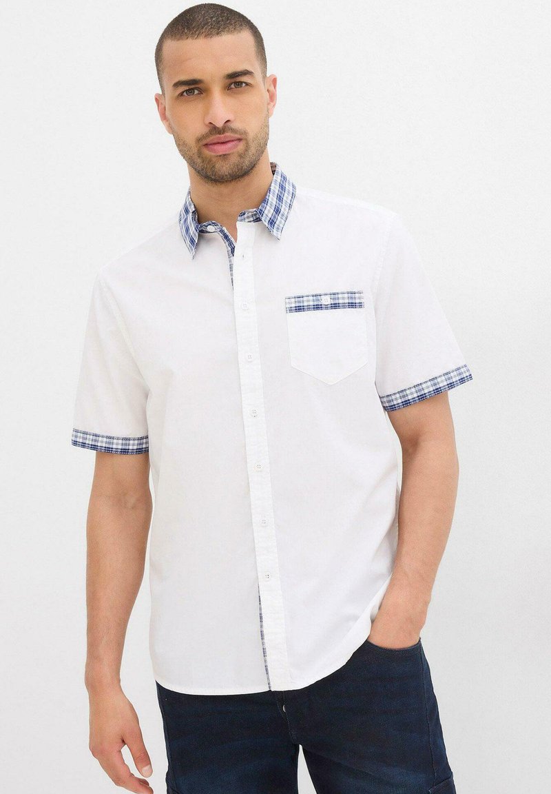 Camicia bianca a maniche corte con colletto e polsini a quadri blu e bianchi. Presenta una piccola tasca sul petto, chiusura con bottoni e tessuto in cotone.