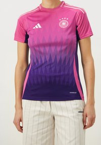 Damska koszulka sportowa Adidas z gradientem od różowego do fioletowego, geometrycznymi wzorami i trzema paskami na ramionach. Oddychający materiał.