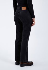 Jeans in denim nero con vita alta, dotati di un'etichetta in pelle marrone sul retro, taglio dritto e dettagli di cucitura minimi.