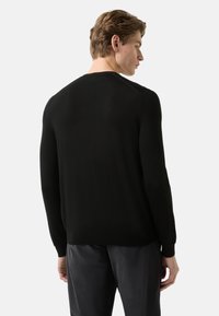 Černý svetr s kulatým výstřihem, dlouhými rukávy a žebrovanými manžetami. Materiál působí měkce a hladce, s přiléhavým střihem.