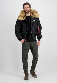 Crna bomber jakna s lažnom krznom kapuljačom, uparena s maslinasto zelenim cargo hlačama i smeškim tenisicama. Ima patentne zatvarače i više džepova.