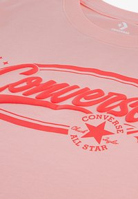 Ροζ βαμβακερό μπλουζάκι με μεγάλο κόκκινο λογότυπο "Converse", με αστέρια και κείμενο "All Star", σε ματ, λείο φινίρισμα.