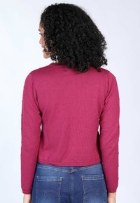 Magenta, strukturiertes Strickpullover mit langen Ärmeln, im cropped Design und gepunktetem Muster; kombiniert mit Jeans.