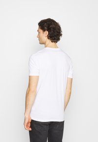 T-shirt blanc à manches courtes en coton, avec un col rond et une coupe décontractée, présenté sur une personne de dos, portant un jean foncé.