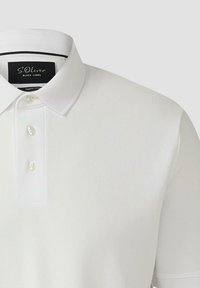 Polo blanc avec trois boutons et un col classique, avec une étiquette noire à l'intérieur de l'encolure.