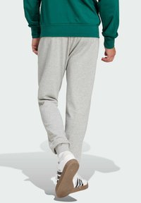 Sive hlače od treninga opuštenog kroja s suženim manžetama, uparene s bijelim tenisicama koje imaju crne akcentne detalje i teksturirane gumene potplate.