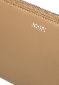 Portafoglio in pelle marrone chiaro con una texture liscia, cuciture visibili e una cerniera argentata. Il logo del marchio "JOOP!" è stampato in bianco.