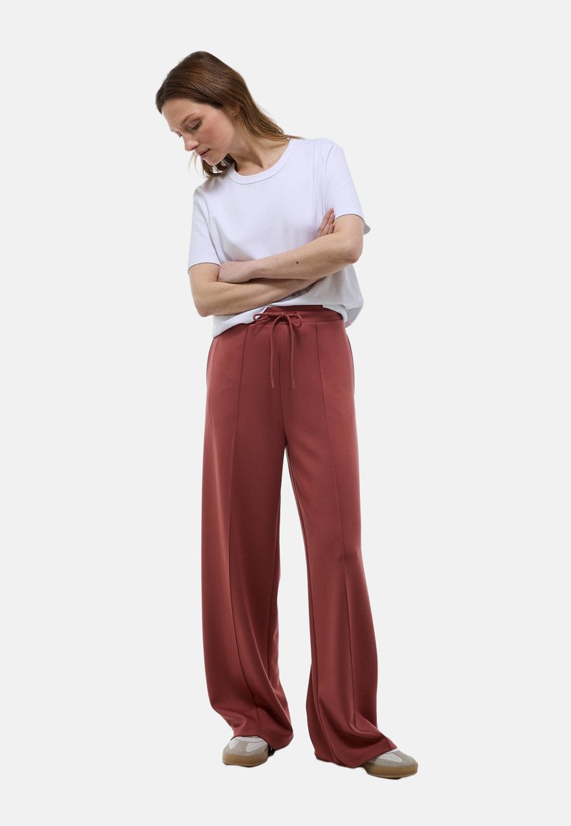 T-shirt blanc à manches courtes associé à un pantalon large à taille haute de couleur rouille avec un cordon de serrage et des jambes larges.