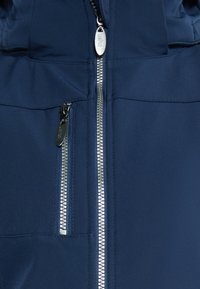 Námořnická modrá bunda s hladkým povrchem, která má centrální zip a boční kapsu. Zip má kovové detaily pro zvýšení odolnosti.