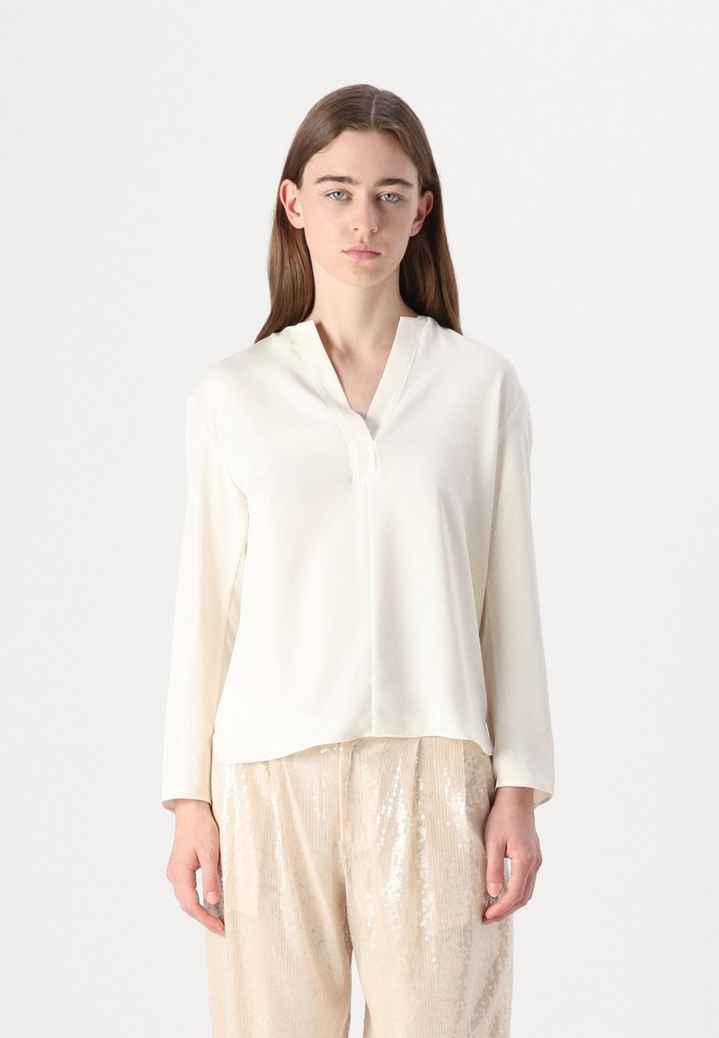 Blusa di colore crema chiaro con scollatura a V,maniche lunghe e una texture liscia. Abbinata a pantaloni beige con paillettes, che presentano un leggero luccichio.