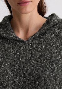 Pull en tricot gris avec capuche, arborant une surface texturée et un col côtelé, offrant une apparence confortable et décontractée.