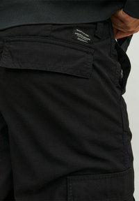 Pantaloni cargo neri realizzati in tessuto resistente, con una tasca posteriore, cuciture visibili e un'etichetta con il marchio vicino alla vita.