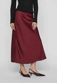 Jupe A-line en satin bourgogne avec une texture lisse, fente sur le côté, et haut noir à manches longues côtelé, assortie avec des escarpins à talons pointus foncés.
