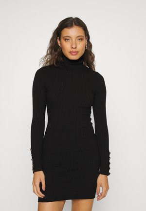 Robe turtleneck noire à côtes avec manches longues, présentant cinq boutons décoratifs sur les poignets. Ajustement slim et longueur genou.