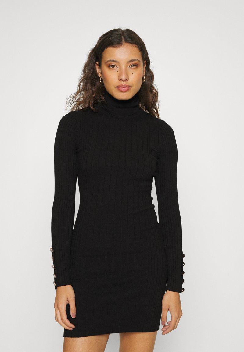 Robe turtleneck noire à côtes avec manches longues, présentant cinq boutons décoratifs sur les poignets. Ajustement slim et longueur genou.