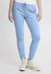 Hele hallid jogger püksid elastse vöökoha ja nööriga, küljetaskudega ja kitsenevate jalgadega, koos valgete kõrgetega spordijalatsitega.