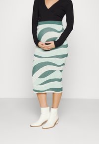 Pletená tužková sukně s azurovým a bílým vlnkovaným vzorem, vysokým pasem, v kombinaci s bílými kotníkovými botami s blokovým podpatkem.