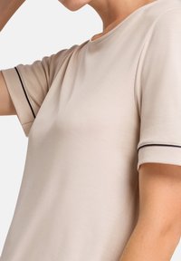 T-shirt beige con scollatura rotonda e maniche corte, caratterizzato da bordi blu scuro sui polsini. Tessuto liscio e leggero con una vestibilità comoda.