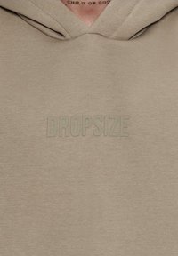 Hættetrøje i lys beige stof med en blød tekstur. Har et fremtrædende "DROPSIZE" logo i matchende prægede bogstaver.