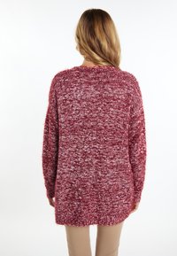 Pulover lung și larg, de culoare burgundă, tricotat, cu o textură pufoasă și stropi albi. Are un decolteu rotund și umeri căzuți.