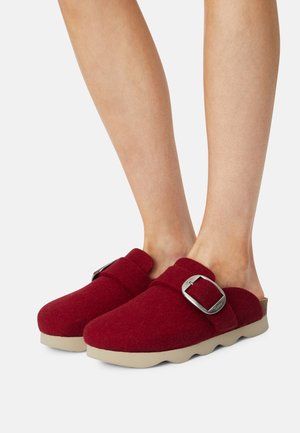 Red felt clogs with a rounded toe, a strap featuring a silver buckle, and a beige rubber sole. Textured wool-like surface.