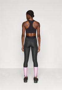 Sort atletisk crop top, højtaljede sorte leggings med pink detaljer ved de nederste ben, glat tekstur, racerback design.