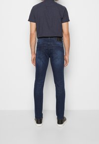 Slim fit tmavě modré džíny s hladkým denimovým vzhledem, se zadními kapsami a koženou nášivkou na pase.