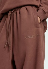Bruna bomullssweatpants med elastisk midja, dragsko, sidofickor och en präglad adidas-logga på framsidan.