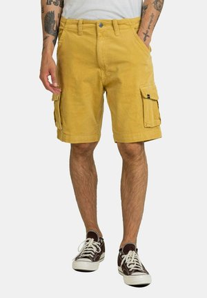 Yellow corduroy cargo shorts with front pockets and side flap pockets. Worn with dark sneakers, featuring a casual fit and textured fabric.