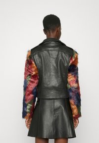 Giubbotto di pelle nera con maniche in pelliccia sintetica colorata nei toni rosso, verde e blu. Presenta una vestibilità aderente e un colletto classico.