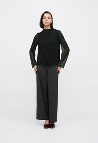 Μαύρο τοπ με διάφανα μακριά μανίκια, συνδυασμένο με σκούρο παντελόνι φαρδιάς γραμμής. Το ύφασμα φαίνεται ελαφρύ, προσφέροντας ένα απαλό, υφασμένο φινίρισμα.