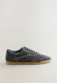 Tenis gri din nubuc cu o textură netedă, vârf rotund și talpă din cauciuc de culoare deschisă, în contrast. Prezintă un design clasic cu șireturi și accente laterale.