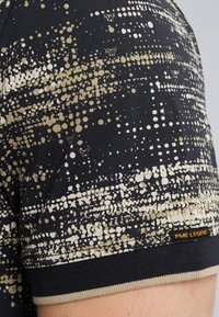 Zwart shirt met korte mouwen, voorzien van een textuurpatroon van gouden en crème stippen, met een PME Legend-label en contrasterende beige afwerking op de mouw.