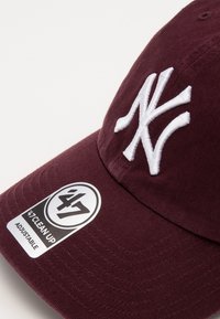 Gorra de béisbol burdeos hecha de algodón con el logo NY bordado en blanco, visera curvada y una etiqueta ajustable en blanco y negro.