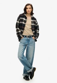 Czarna i biała koszula flanelowa w kratę na beżowym podkoszulku, w połączeniu z jasnoniebieskimi luźnymi dżinsami i czarnymi butami. Swobodny krój z podwiniętymi rękawami.