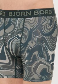 Μπάρες μπάνιου Björk Borg με σχέδιο σε πράσινο, γκρι και μαύρο στροβιλισμό. Διαθέτει φαρδύ μαύρο λάστιχο με το όνομα της μάρκας σε πράσινο.