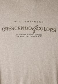 Tela texturada beige con texto gráfico en relieve en marrón oscuro, con la frase "CRESCENDO OF COLORS" acompañada de una línea decorativa.