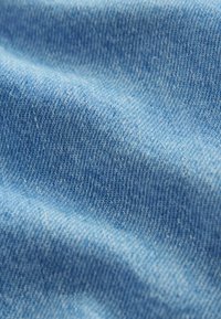 Tela de mezclilla azul claro con una textura suave, que presenta un patrón de tejido de sarga clásico y ligeras variaciones de color en toda su extensión.
