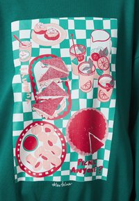 Grafický dizajn na zelenom pozadí zobrazujúci piknikovú scénu so sendvičmi, nápojmi, pečivom a koláčom na pozadí so vzorom šachovnice.