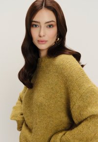 Senfgelber Strickpullover mit strukturiertem Finish, hoher Kragen und lockerer Passform, kombiniert mit großen goldenen Creolen.
