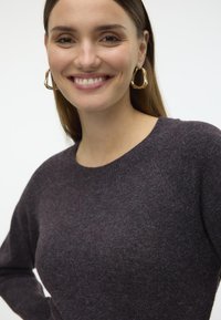 Maglione grigio scuro con scollatura rotonda, tessuto texturizzato e maniche lunghe, abbinato a grandi orecchini a cerchio dorati.