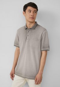 Grijze polo shirt met een kraag, drie knopen en een borstzakje. Heeft contrasterende donkere biezen op de kraag en de mouwen.
