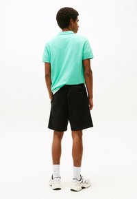 Mintgroene polo en zwarte shorts, met een achterzak, gedragen met witte en zwarte sneakers en witte sokken. Glad stof textuur.