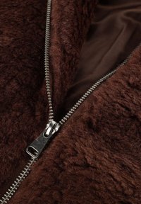 Bruine geweven stof met een fuzzy uitstraling en een metalen rits langs de rand, die een gladde binnenvoering onthult.